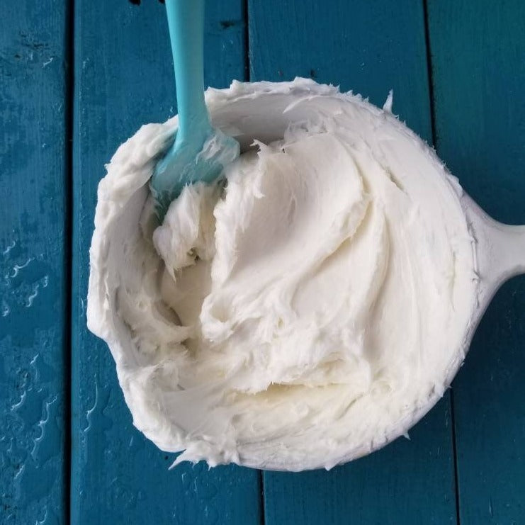 White bowl filled with fluffy just-whipped white body butter on a blue wood table with raindrops